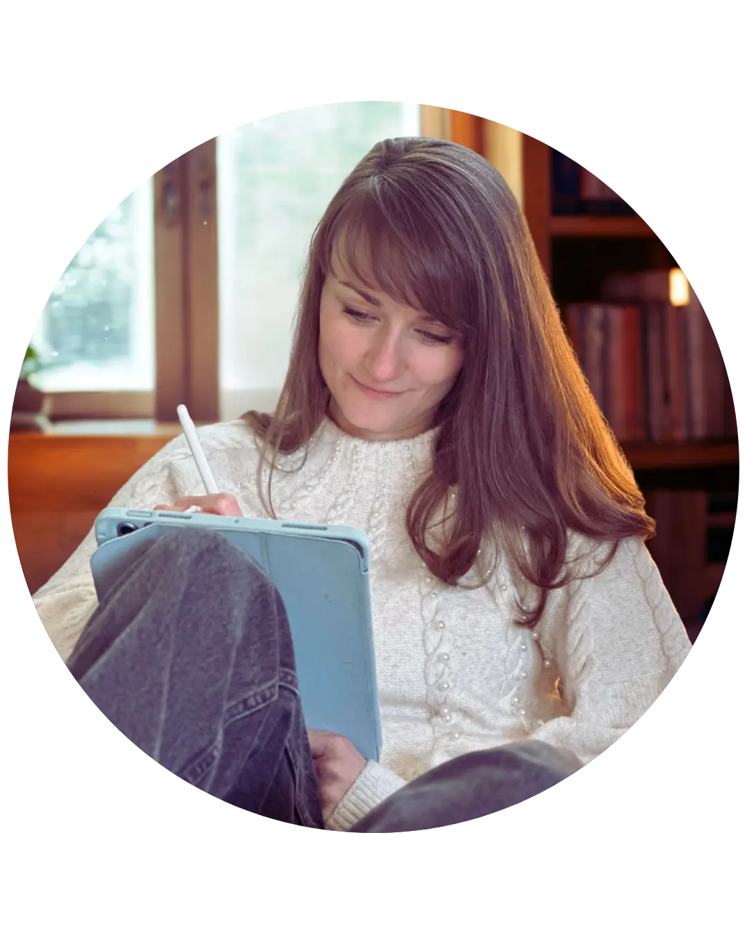 Judith sitz auf einem Sofa, ein Schreibheft in der Hand, in das sie lächelnd etwas notiert. Hinter ihr ein Fenster und ein Regal mit Büchern.